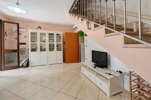 Una sala de estar con televisor, armarios, una escalera y una puerta que da a otra habitación.