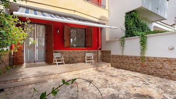 Un edifici residencial amb façana vermella, un balcó i una petita zona de pati amb dues cadires i una taula.