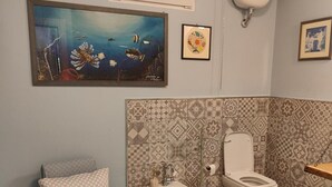 A bathroom with a shower, toilet, bidet, and a sink. There is a painting on the wall and a small shelf with a cup. - Apartment 'Il Melarancio Bb' with Shared Garden, Wi-Fi and Air Conditioning (Monterosi)