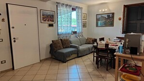 A living room with a sofa, a dining table with chairs, a window with curtains, and a door. - Apartment 'Il Melarancio Bb' with Shared Garden, Wi-Fi and Air Conditioning (Monterosi)