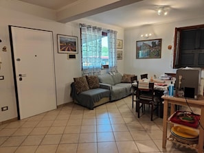 Una sala de estar con un sofá, una mesa de comedor con sillas, una ventana con cortinas y una puerta.