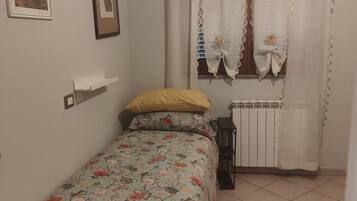 Une chambre à coucher avec un lit, un radiateur, une fenêtre avec des rideaux et des tableaux accrochés au mur.