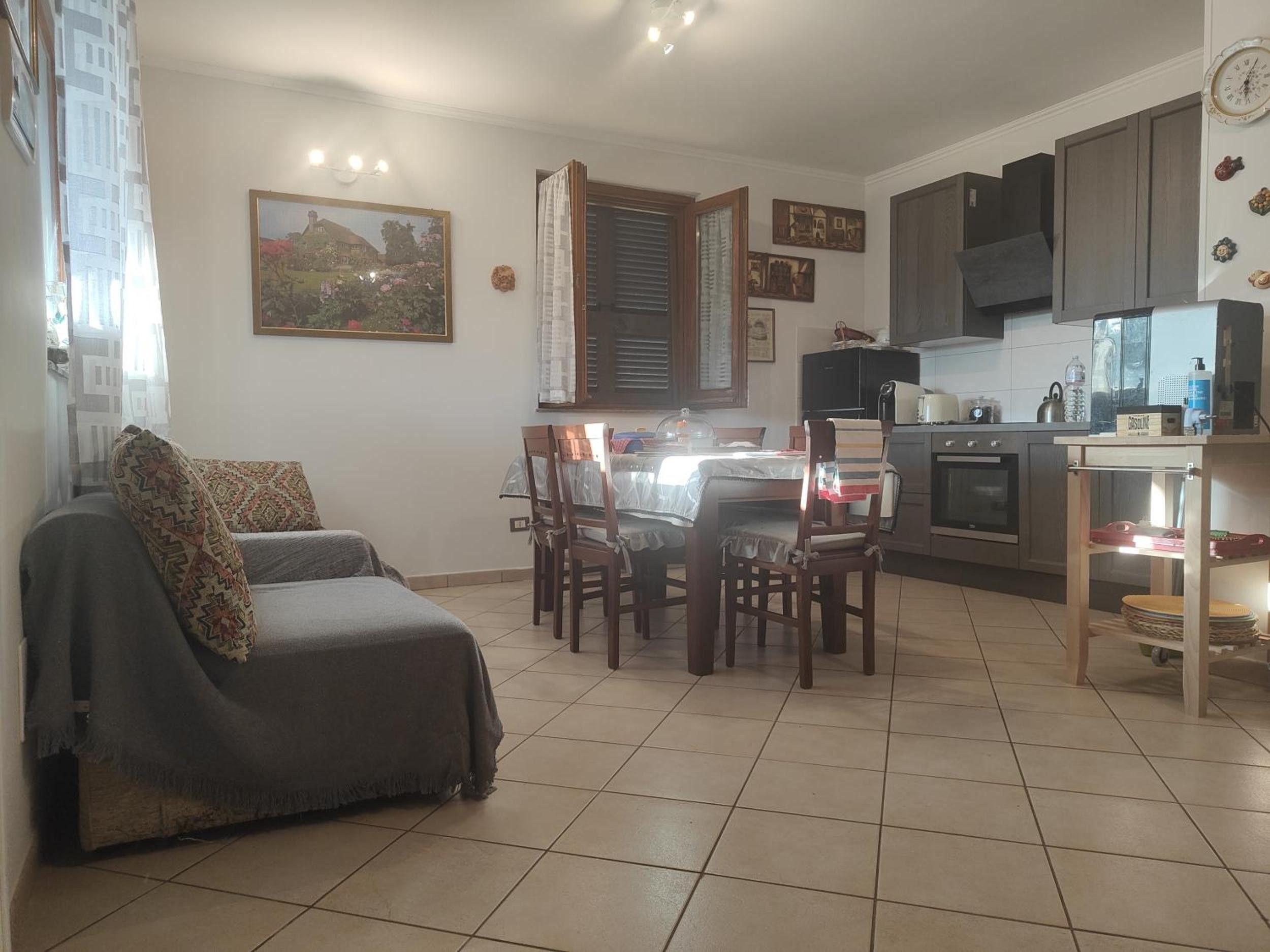 Un salon comprenant un canapé, une table à manger et des chaises. Il y a également un coin cuisine avec des placards et un plan de travail.