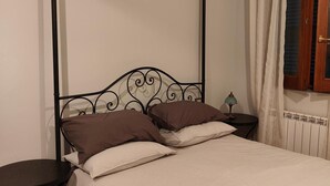 A single bed with a metal headboard, two pillows, a bedside table with a lamp, and a window with curtains. - Apartment 'Il Melarancio Bb' with Shared Garden, Wi-Fi and Air Conditioning (Monterosi)