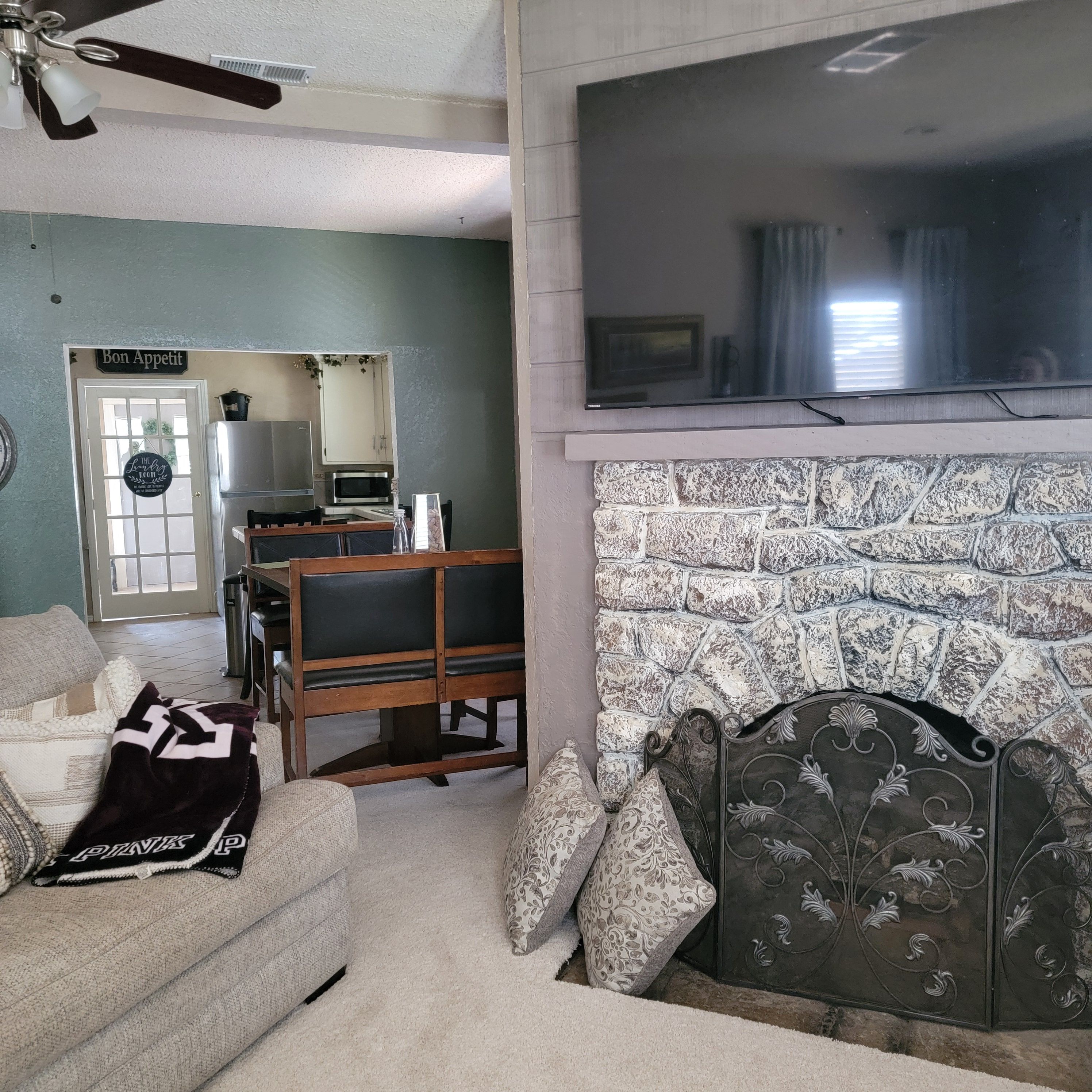 Una sala de estar con chimenea, un televisor montado encima, un sofá y un comedor con mesa y sillas.