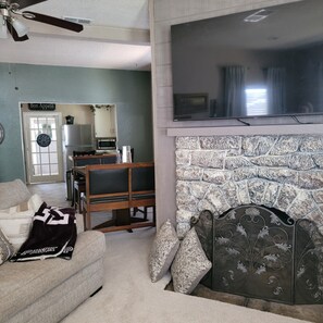 A living room with a fireplace, a television mounted above it, a sofa, and a dining area with a table and chairs. - Welcoming 2-bedroom house with AC in charming Post Texas. Good quite neighbor (Post)