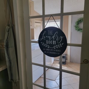 A door with a circular sign that reads 'The Laundry Room' and a note about tipping for change left in pockets.