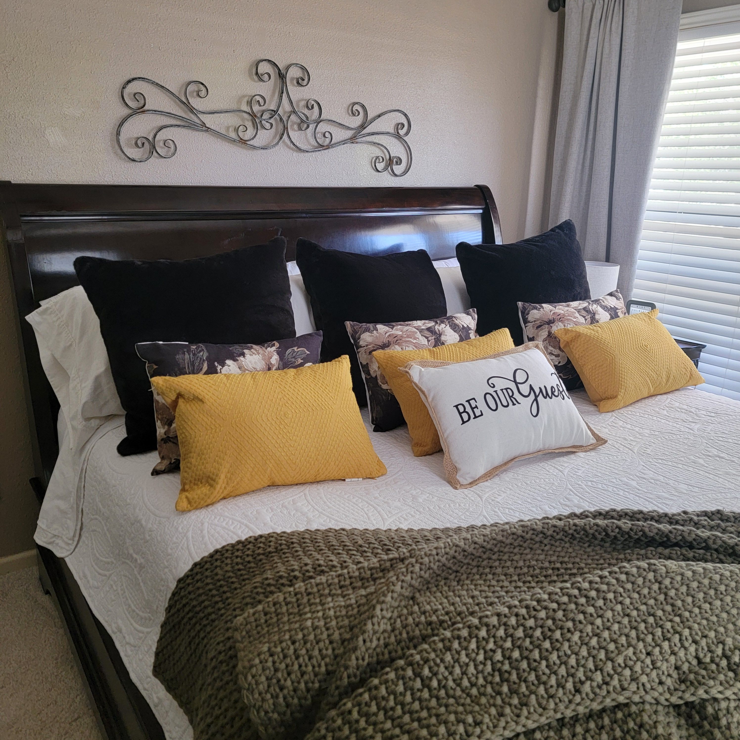 Una cama con cabecera, varios almohadones y un adorno en la pared.