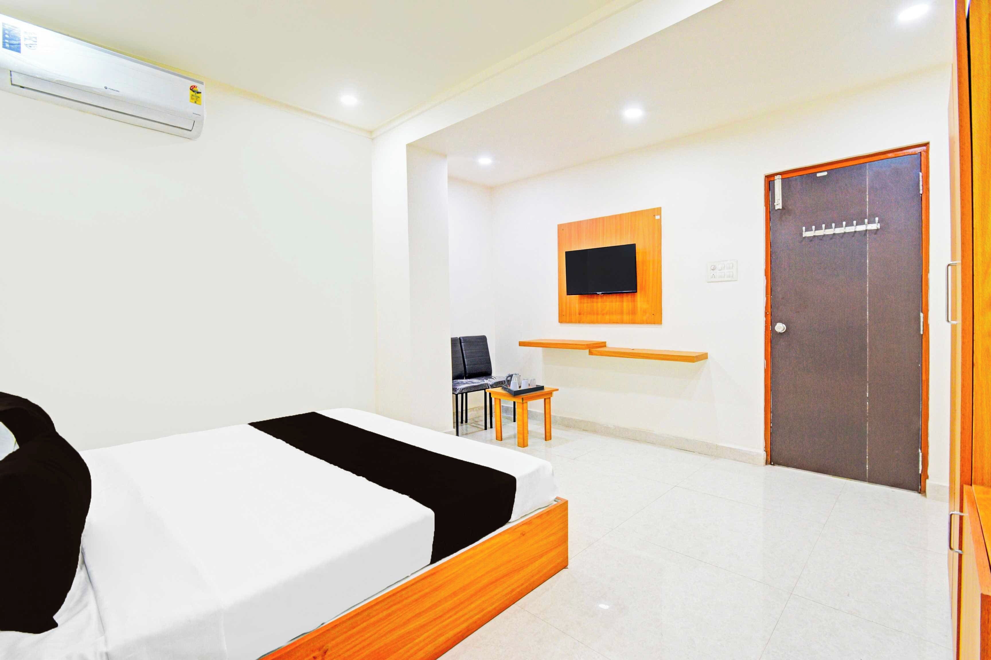 Una habitación de hotel con una cama, un escritorio, una silla, un televisor montado en la pared y una puerta.