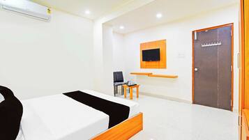 Una habitación de hotel con una cama, un escritorio, una silla, un televisor montado en la pared y una puerta.