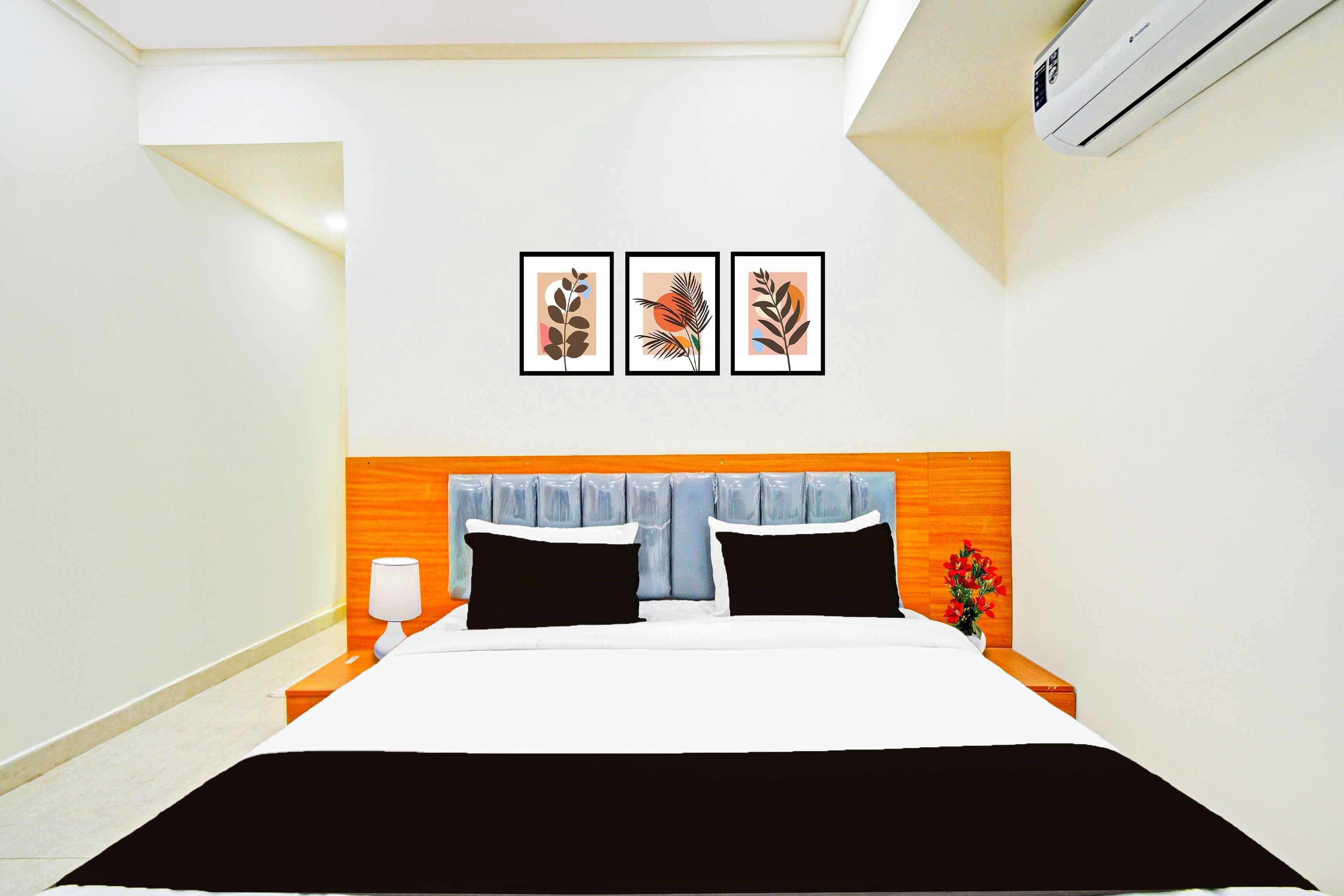A hotel room with a bed, a nightstand, a lamp, and three framed artworks on the wall.