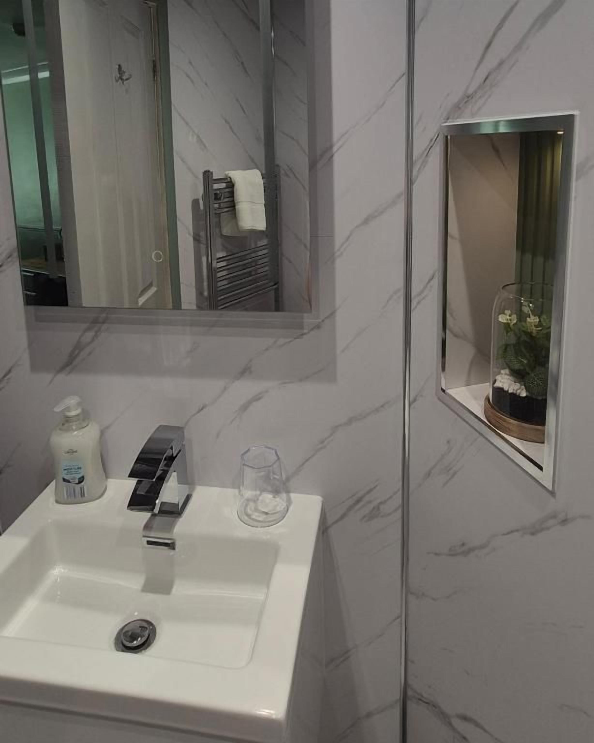 Un baño con un lavabo blanco, un espejo, un vaso y un pequeño florero con flores.