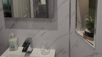 Un baño con un lavabo blanco, un espejo, un vaso y un pequeño florero con flores.