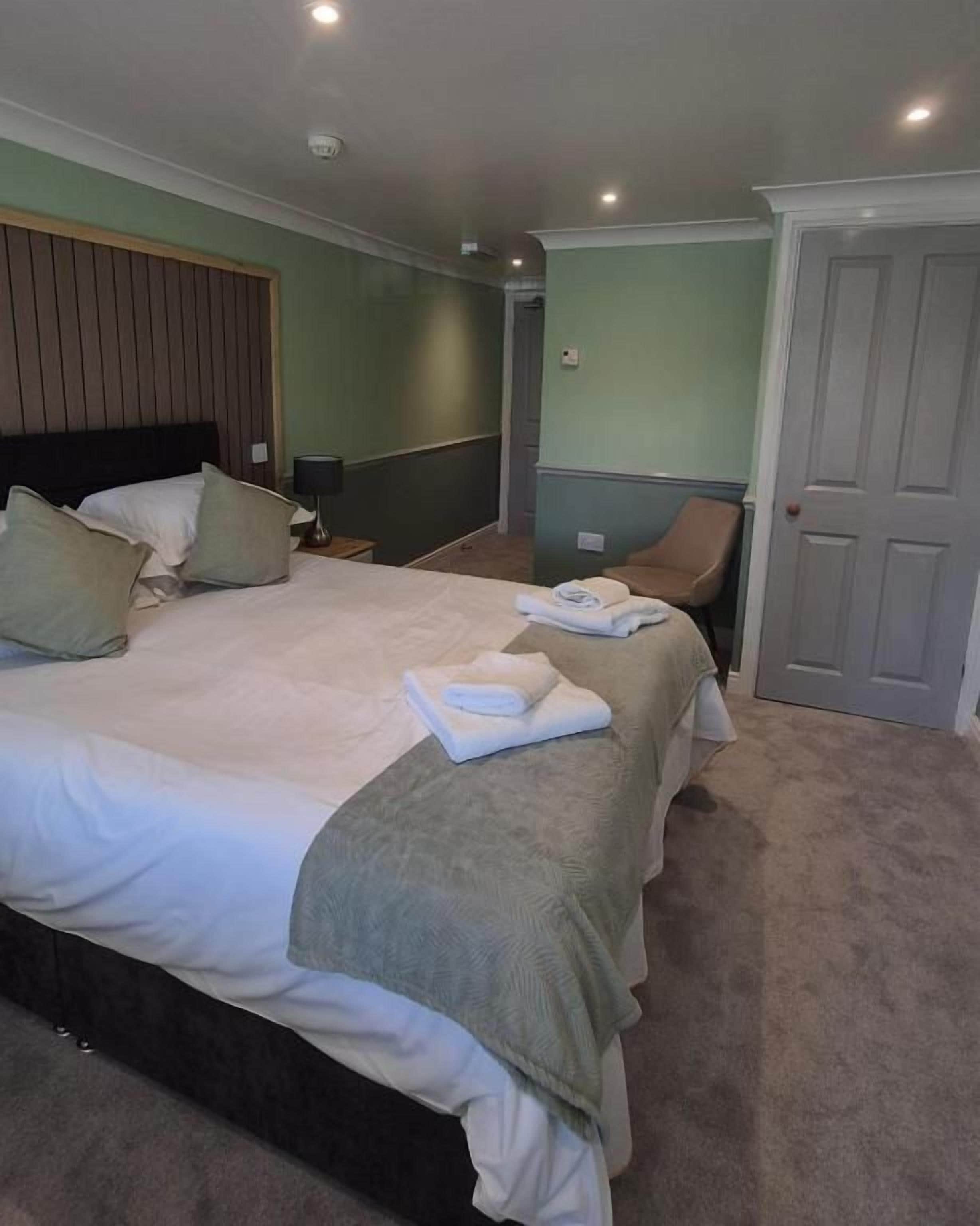 A hotel room with a bed, a chair, a door, and a nightstand.
