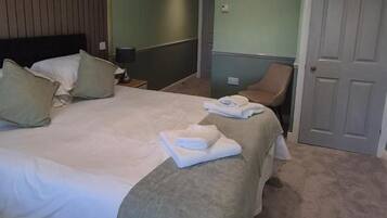 A hotel room with a bed, a chair, a door, and a nightstand.
