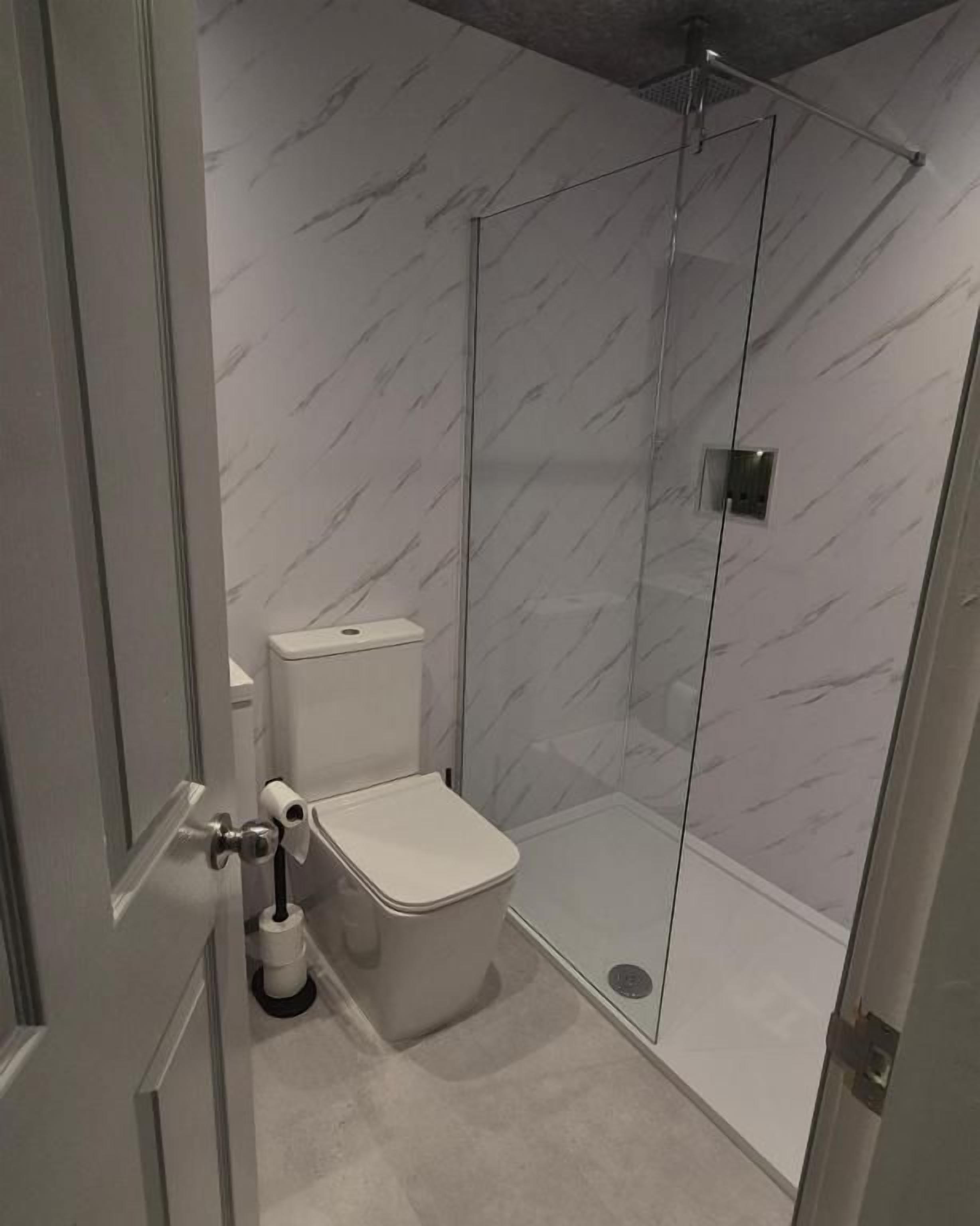 A bathroom with a toilet, a shower enclosure, and a marble-patterned wall.