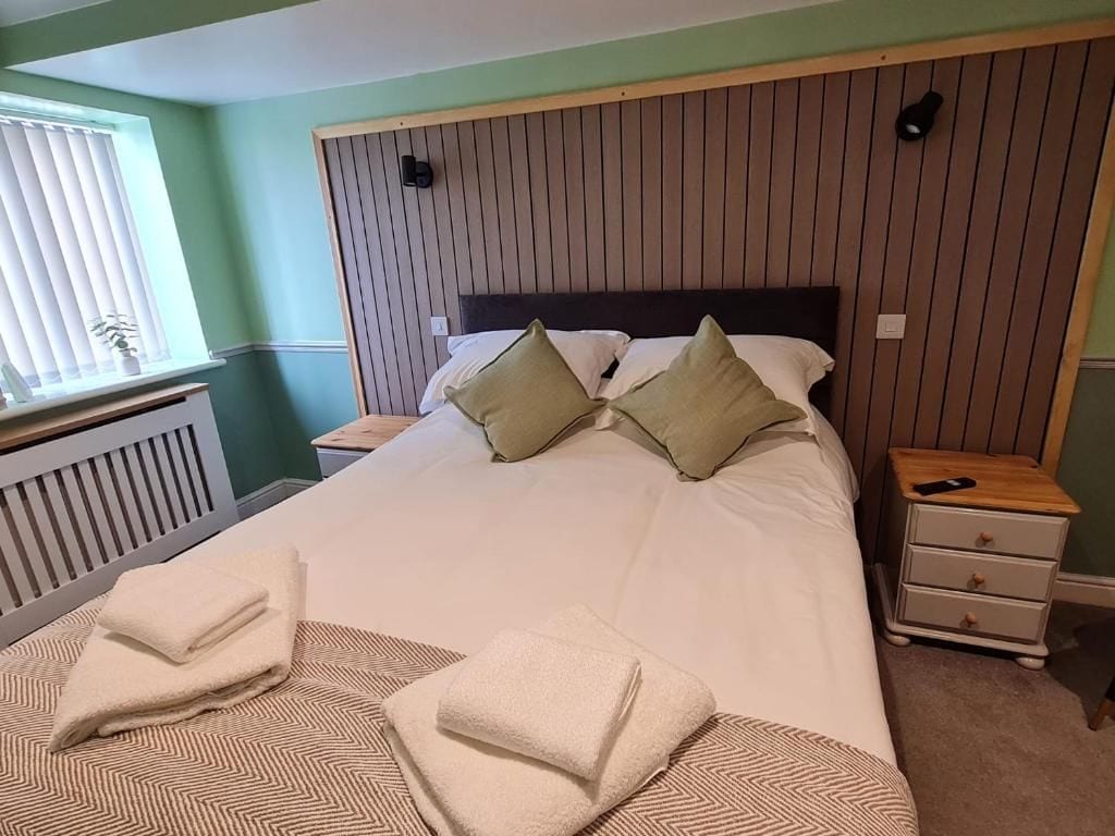 A neatly made bed with pillows, a bedside table with a lamp, and a nightstand with a phone.