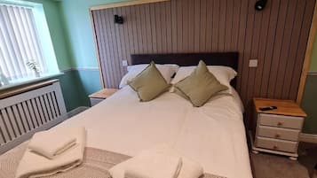 A neatly made bed with pillows, a bedside table with a lamp, and a nightstand with a phone.