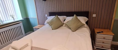 A neatly made bed with pillows, a bedside table with a lamp, and a nightstand with a phone.