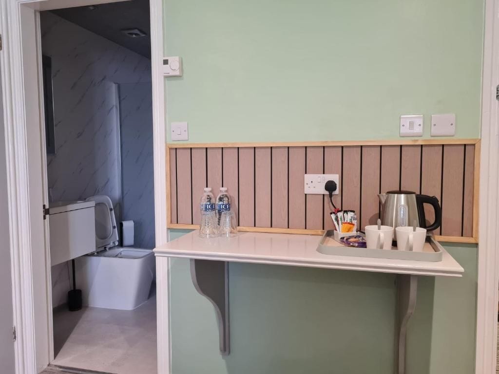 A kitchenette with a countertop, a kettle, cups, and bottles.
