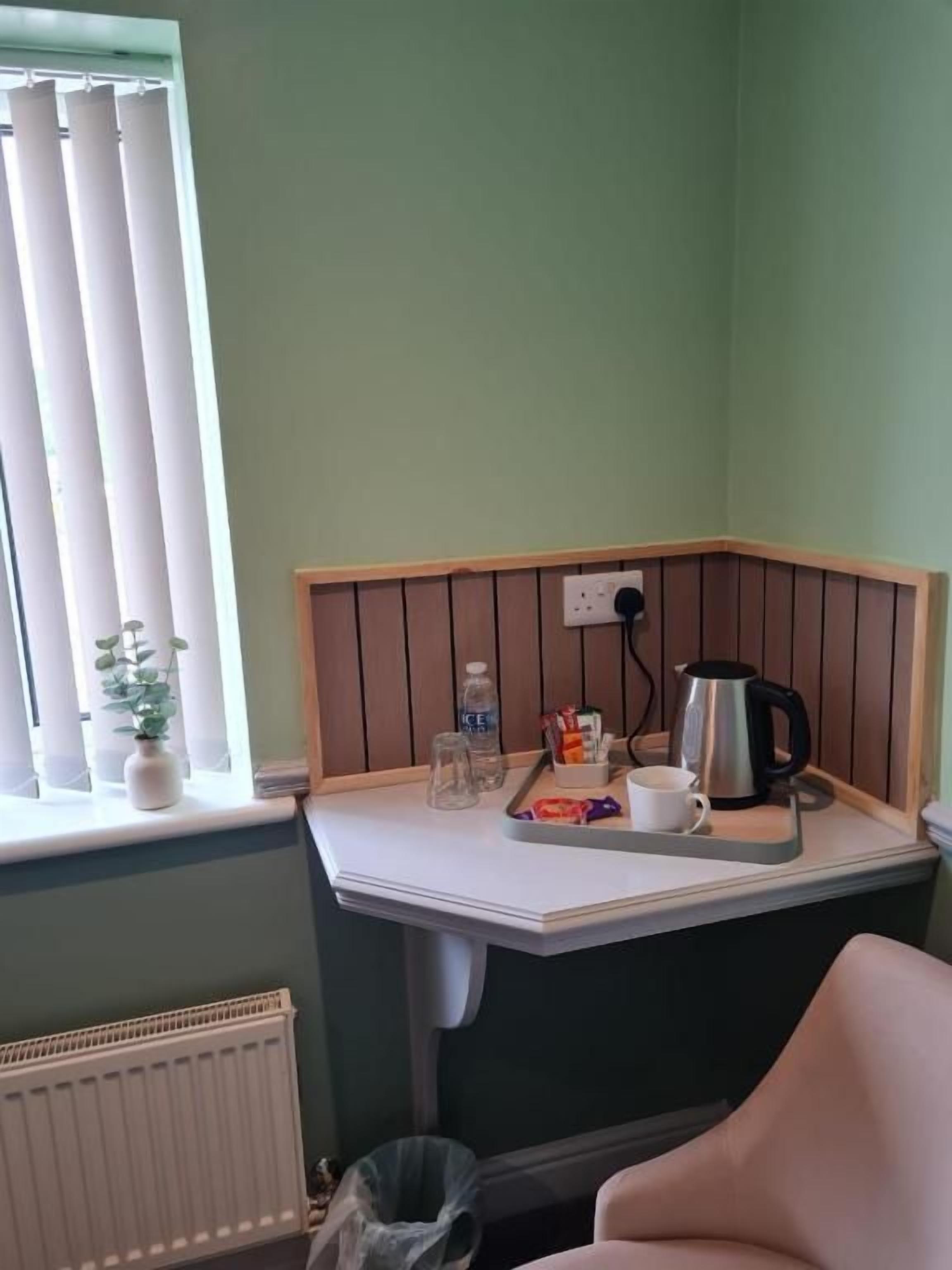 A corner kitchenette with a window, a radiator, a trash bin, and a chair.