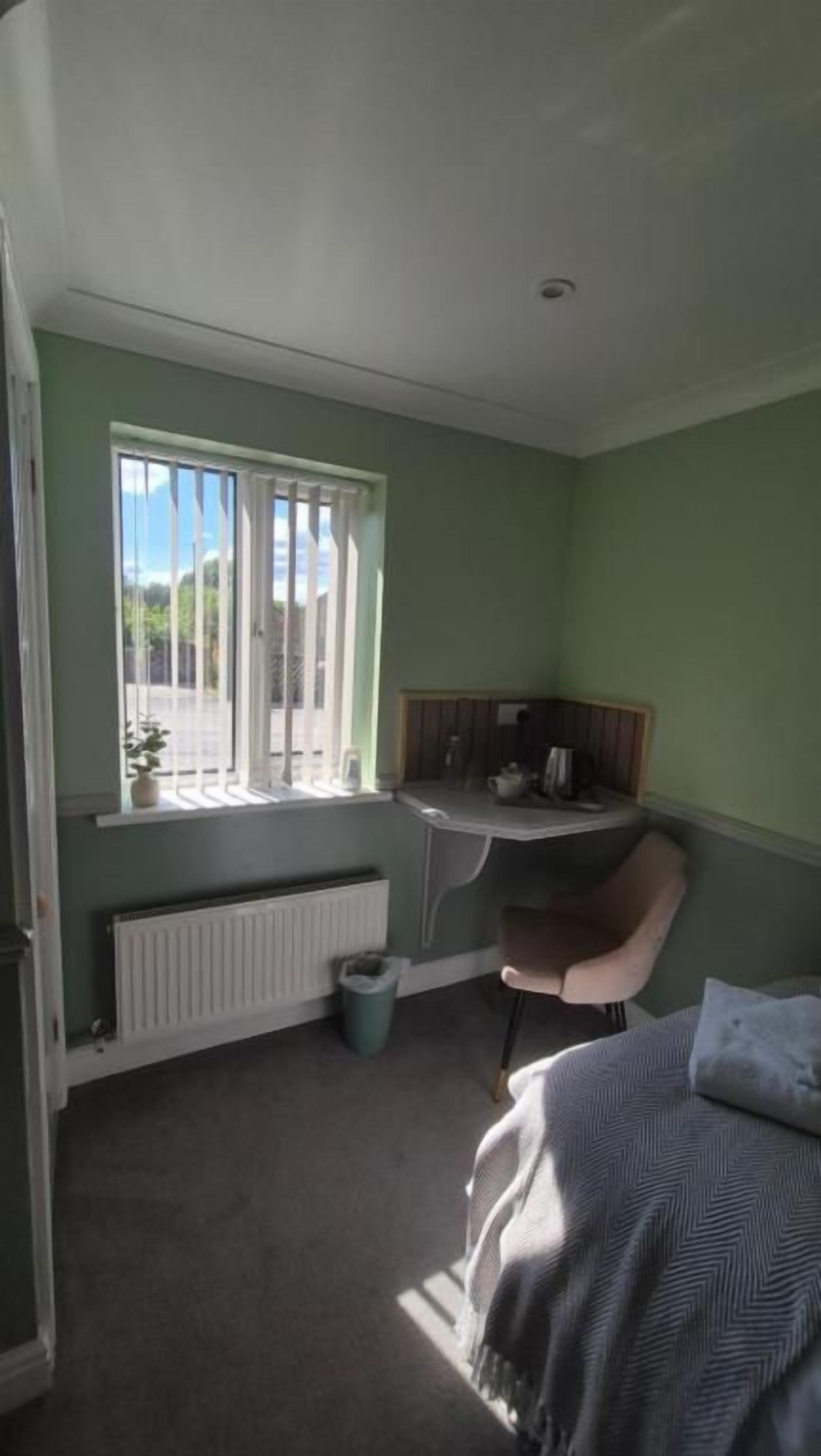 A room with a bed, a desk, a chair, a radiator, and a window.