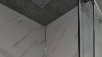 Ducha con puerta de cristal y pared de mármol.
