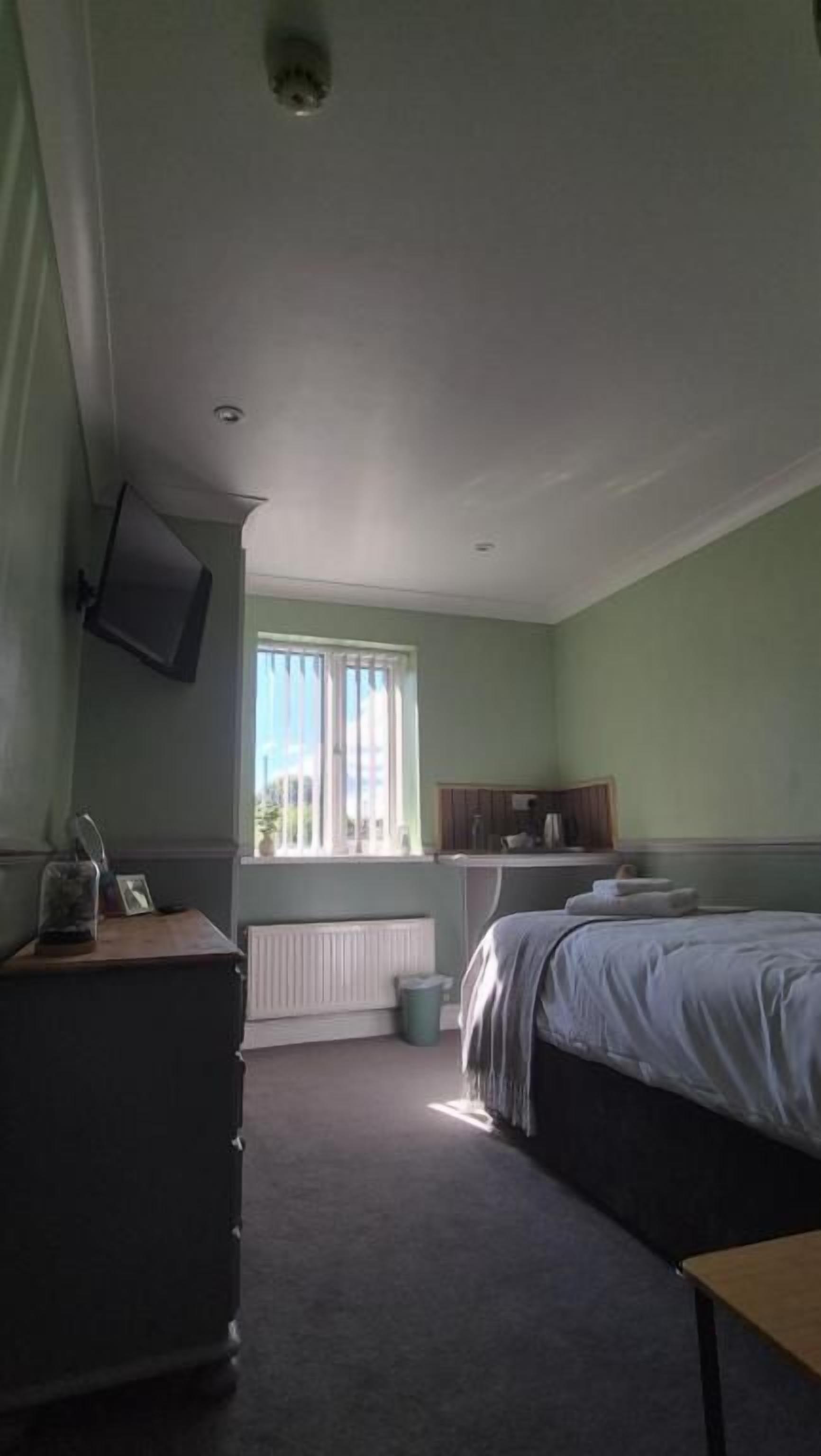 A bedroom with a bed, dresser, and a window with blinds.