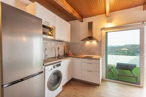 A modern kitchen with a built-in washing machine, a large window, and a view of a green landscape.