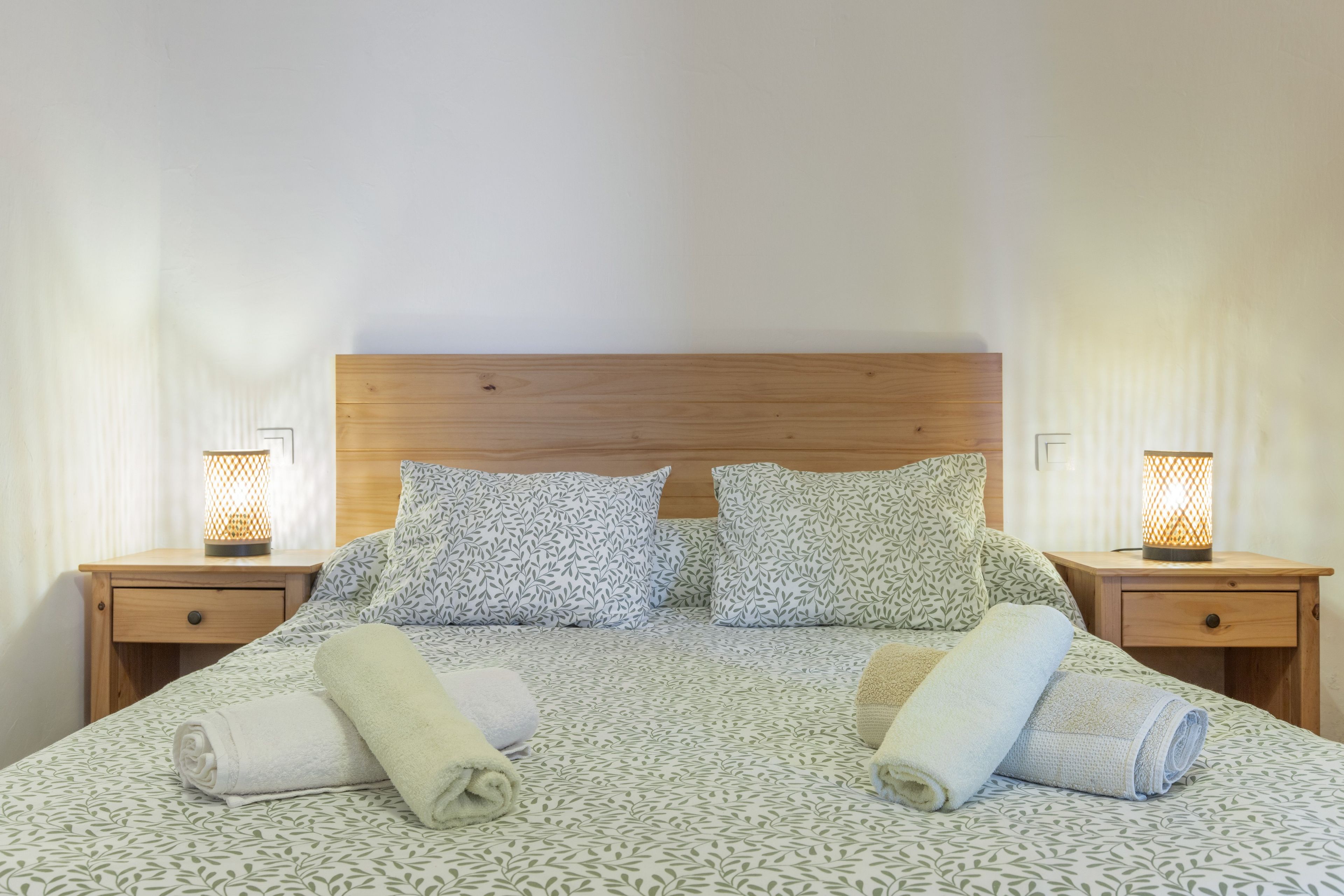 Een netjes opgemaakt bed met beddengoed met een patroon, twee nachtkastjes met lampen, en een houten hoofdbord.