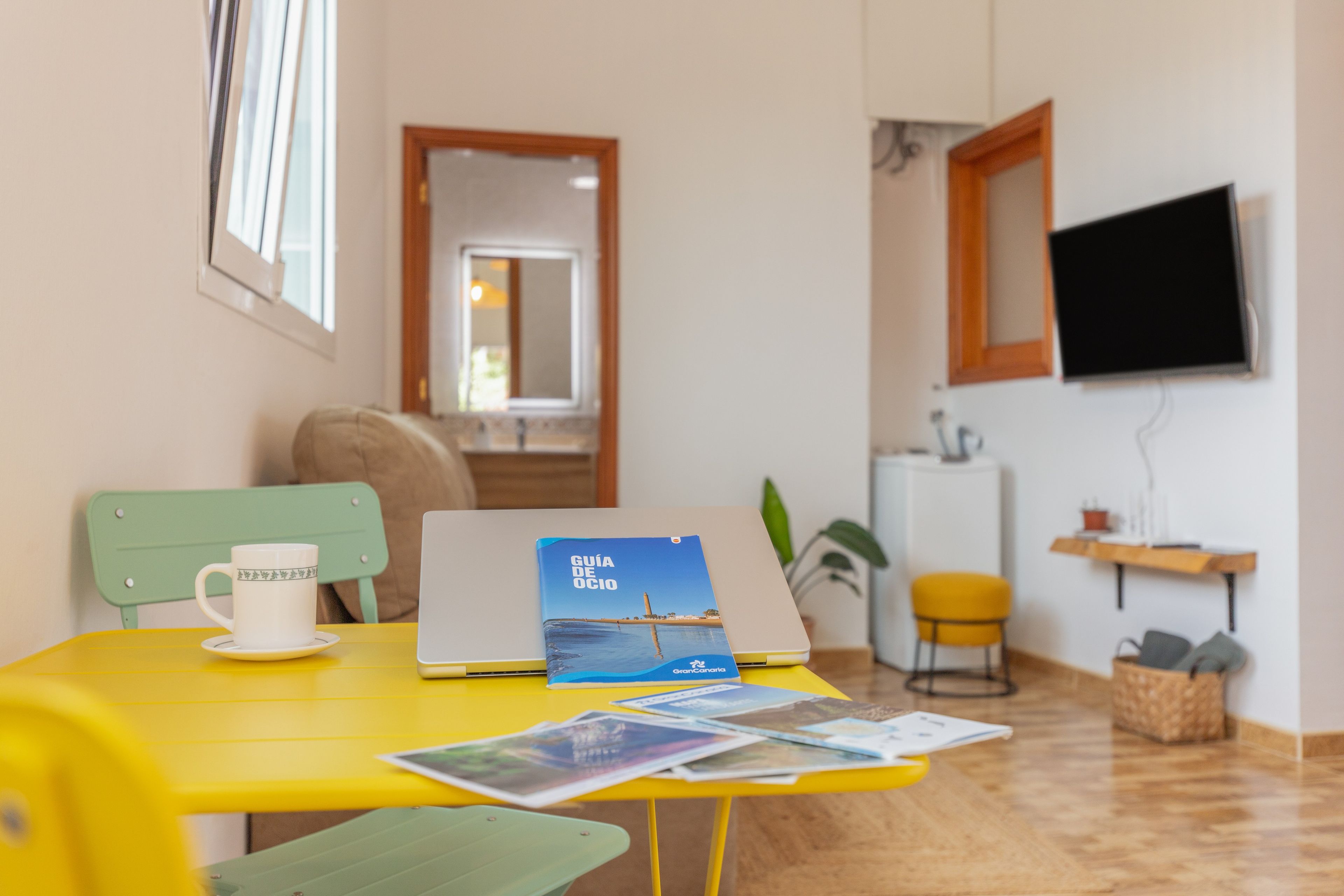 Une pièce avec une table jaune, un ordinateur portable, un livre intitulé « Guide des loisirs » et une tasse blanche.