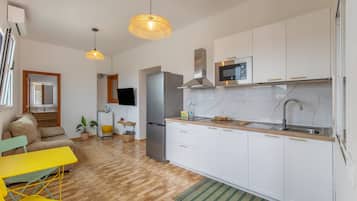 Una cocina moderna con armarios blancos, un refrigerador de acero inoxidable y un microondas. Hay una mesa de comedor de madera y una silla amarilla en la zona de estar.