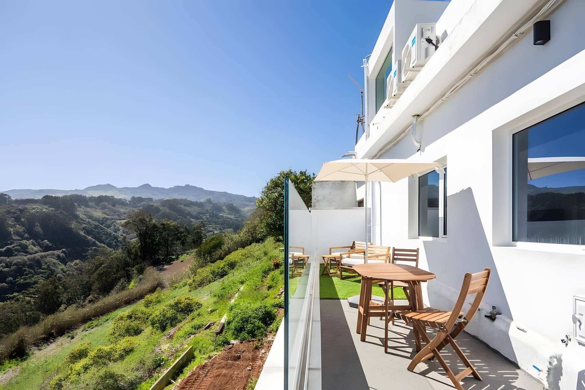 Un balcón con mesa y sillas, con vistas a un paisaje montañoso.