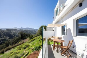 Een balkon met een tafel en stoelen, met uitzicht op een glooiend landschap.