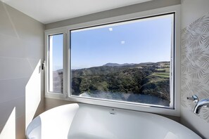 Een badkamer met een groot raam met uitzicht op een vallei en heuvels.