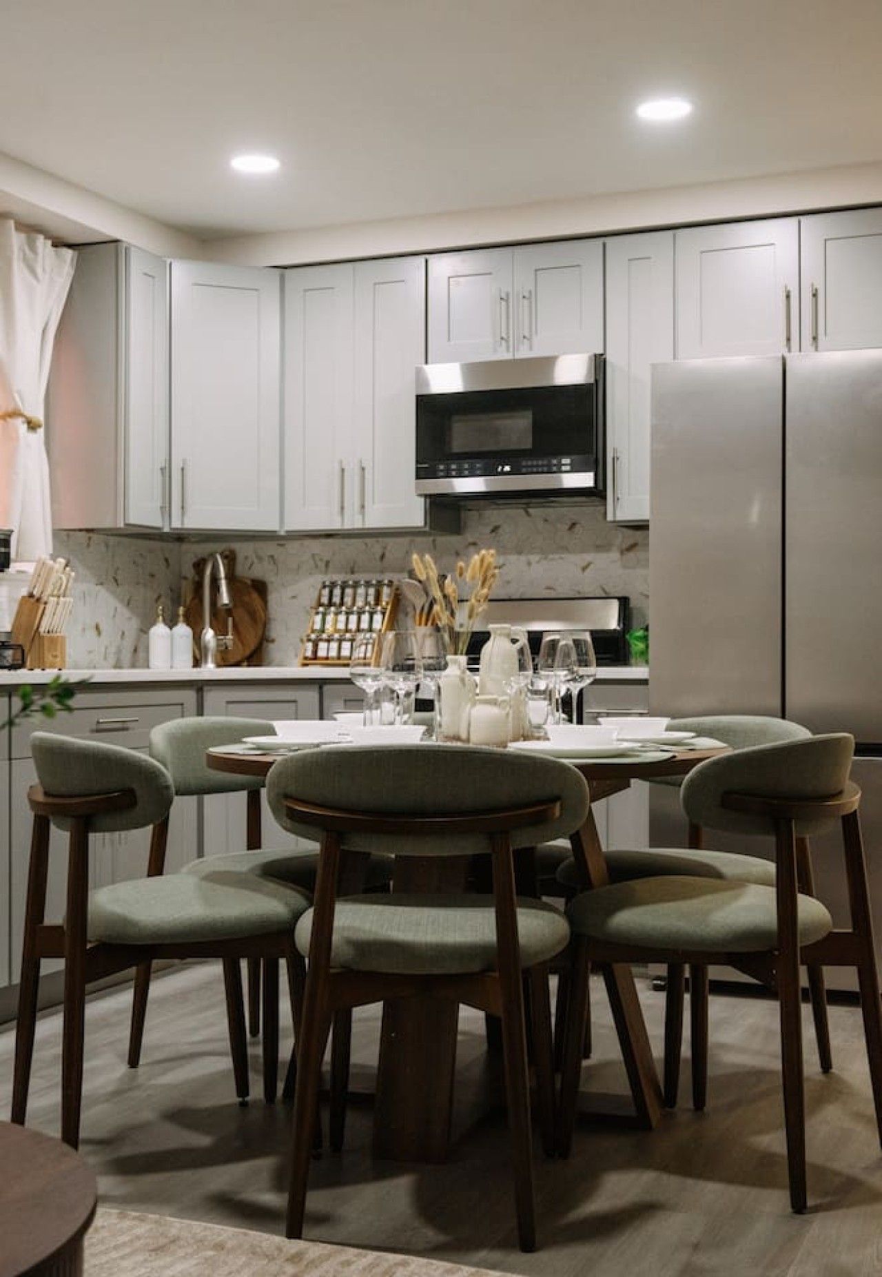 A modern kitchen with white cabinets, a stainless steel refrigerator, and a dining table set for four.