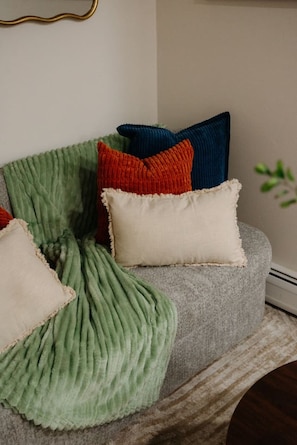 A sofa with a green throw blanket and three pillows in red, blue, and white. - NEW Chic Retreat min NYC & MetLife Private Parking (North Bergen)