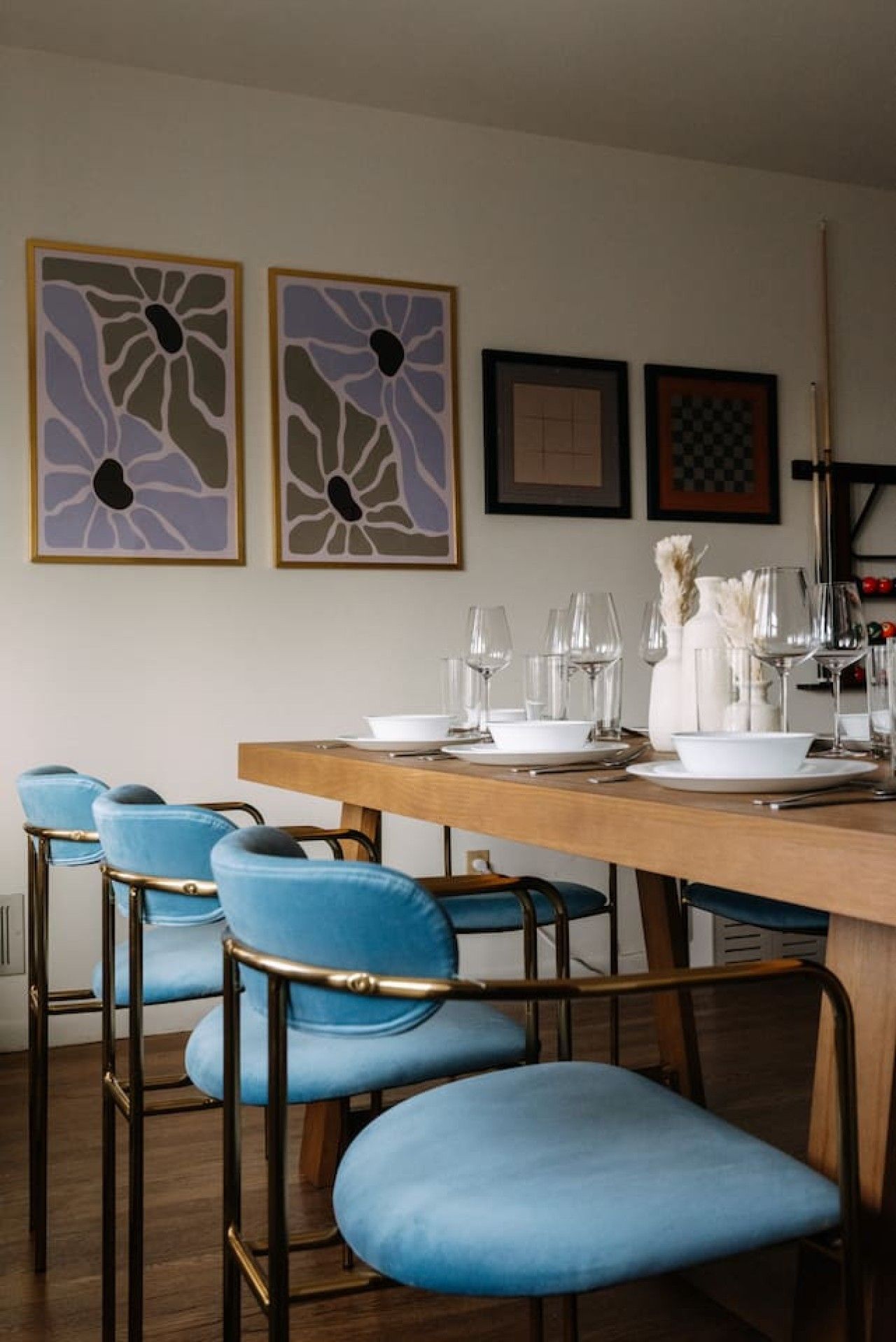 A dining area with a wooden table set for four, blue upholstered chairs, and two abstract wall art pieces.