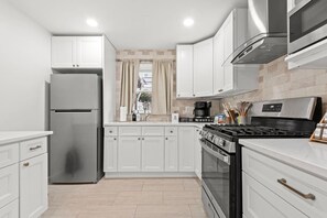 A modern kitchen with white cabinetry, a stainless steel refrigerator, a gas stove, and a coffee maker. - Big City Haven w/Parking 4 Cars & Private Backyard (North Bergen)