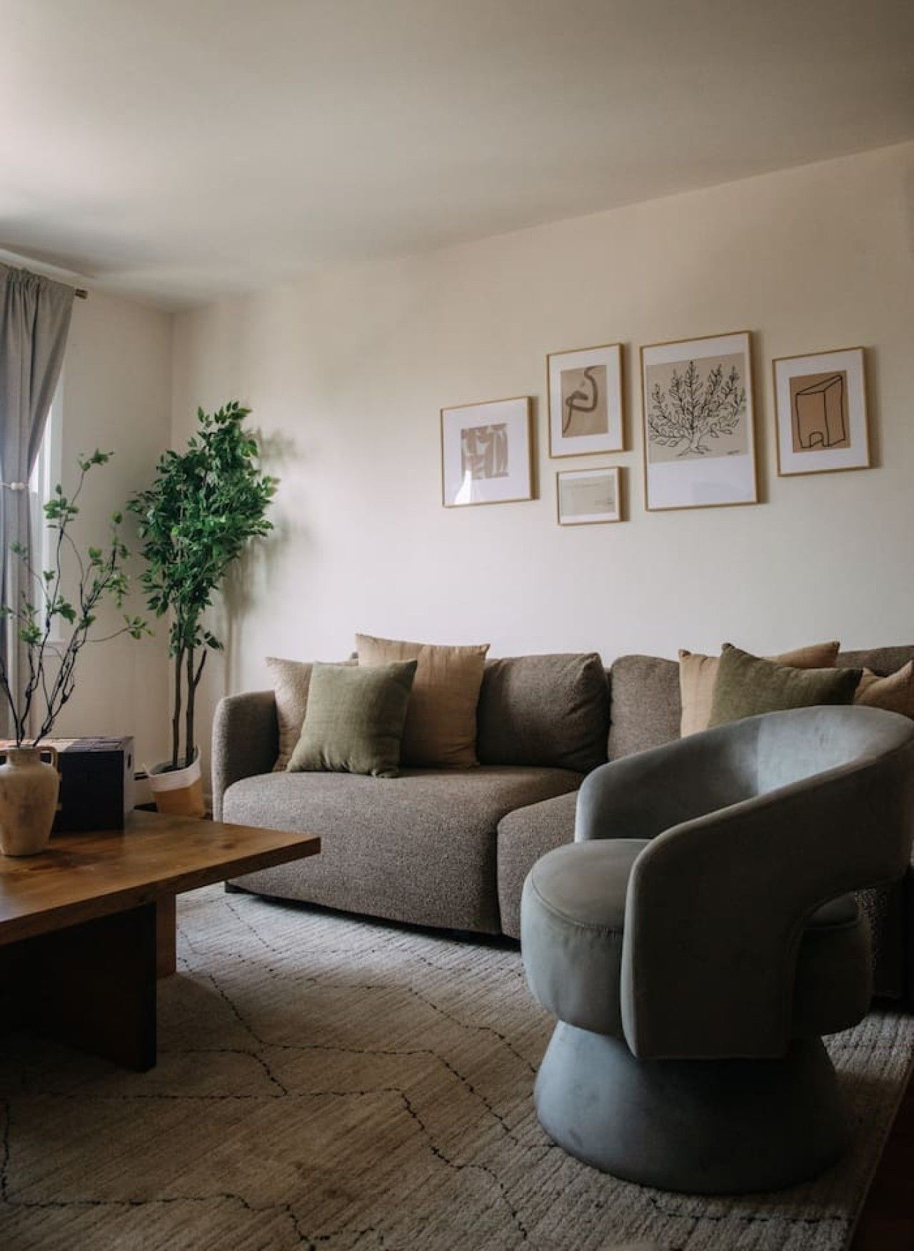 A living room with a sofa, a coffee table, and a chair. There are framed pictures on the wall and a plant on the floor.