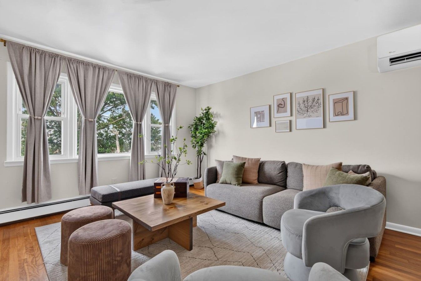 Una sala de estar moderna con sofá, sillones, una mesa de centro y un ventanal con cortinas.
