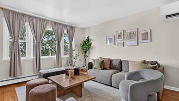 Una sala de estar moderna con sofá, sillones, una mesa de centro y un ventanal con cortinas.