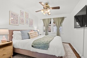 A bedroom with a bed, bedside tables, a ceiling fan, a window with curtains, and wall art. - NEW Spacious w/Parking mins NYC & MetLife (North Bergen)