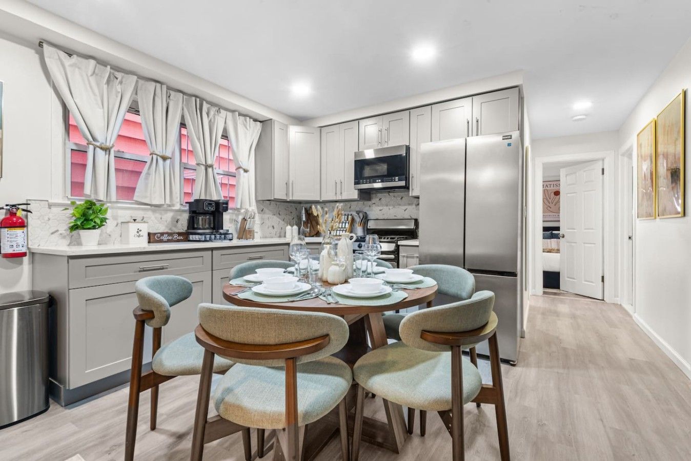 A modern kitchen with stainless steel appliances, a dining area with light blue chairs, and a white color scheme.