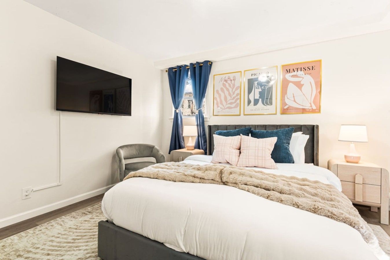 Habitación de hotel con una cama, televisión de pantalla plana, una silla, una mesita de noche y obras de arte en la pared.