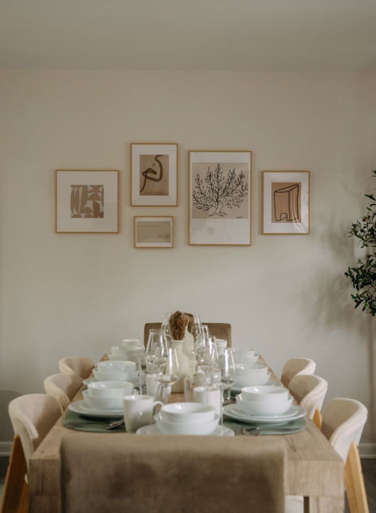 Una mesa de comedor dispuesta con platos y vasos blancos, rodeada de sillas color beige.