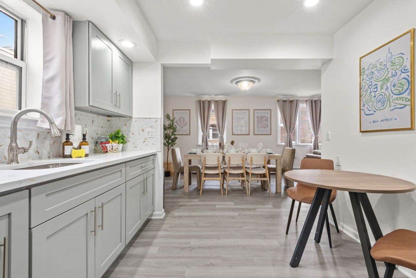 Una cocina moderna con comedor, que incluye una isla central, sillas de madera y un amplio ventanal.