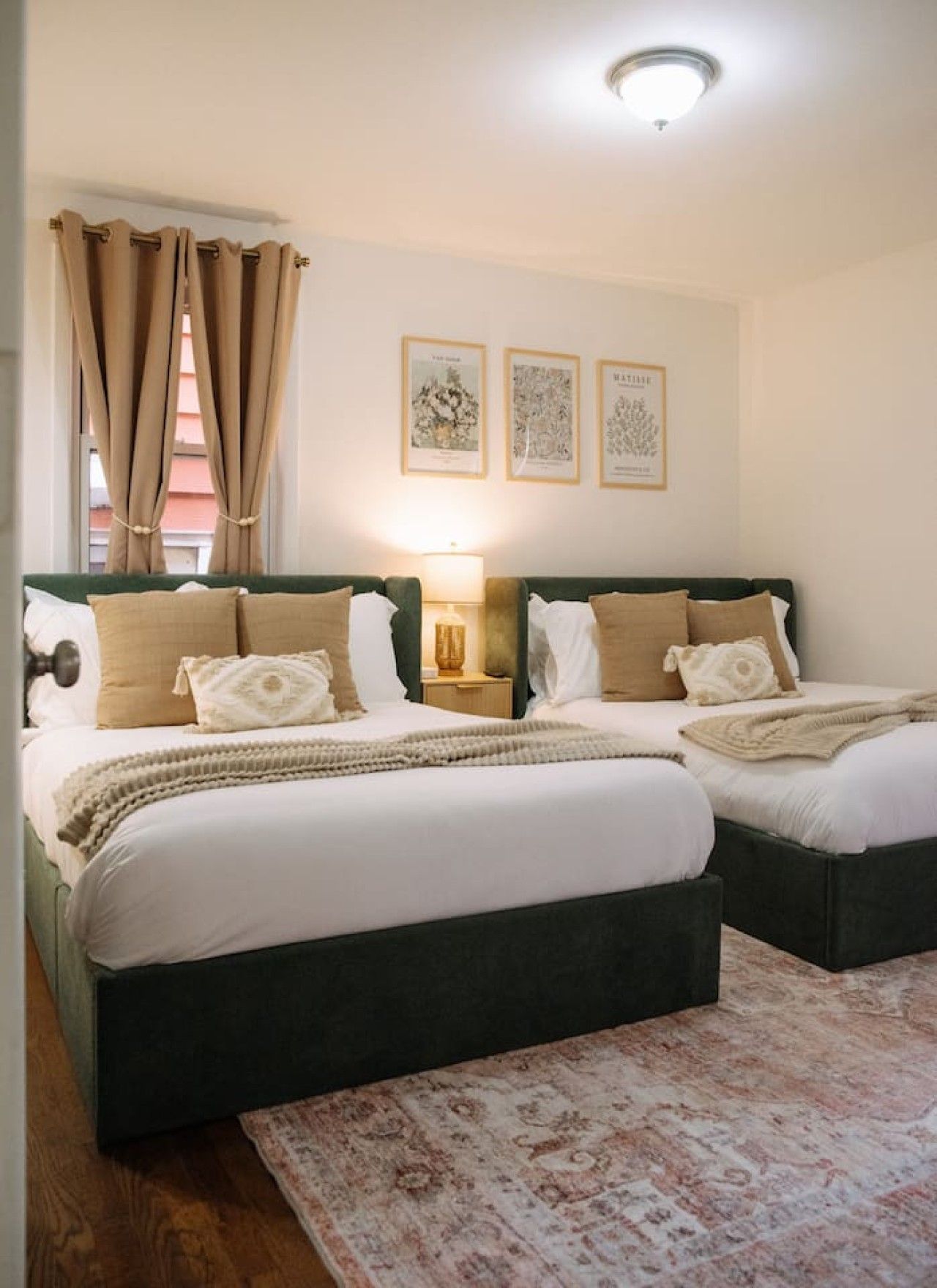 Una cama doble con cabecera verde, una mesita de noche con lámpara y un tapete estampado sobre piso de madera.