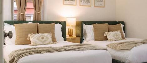 Una cama doble con cabecera verde, una mesita de noche con lámpara y un tapete estampado sobre piso de madera.