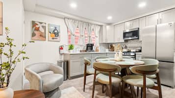 Una cocina moderna con armarios blancos, un refrigerador de acero inoxidable, un microondas y una estufa. Hay una zona de comedor con una mesa redonda y cuatro sillas.
